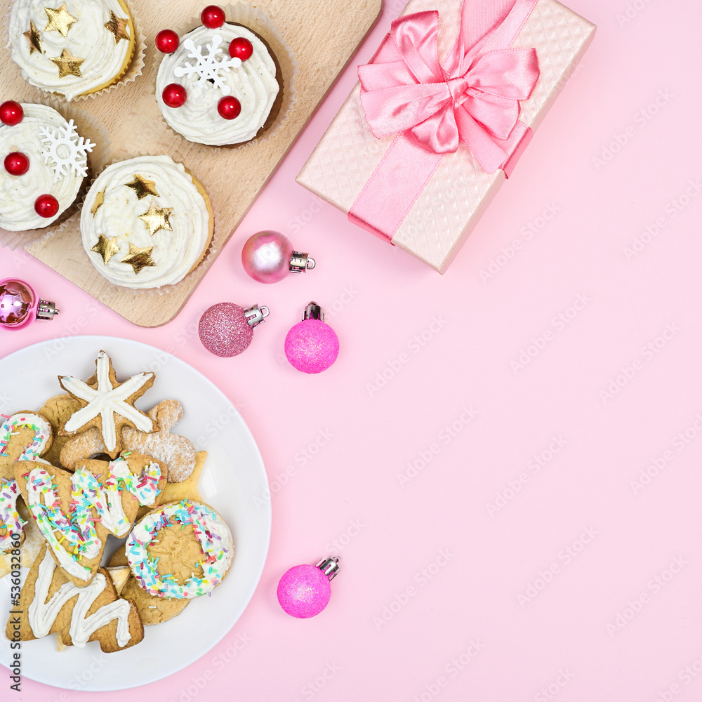 Sweet gingerbread cookes and cup cakes with Christmas ornaments on pastel pink background. Flat lay Sweet gingerbread cookes and cup cakes with Christmas ornaments on pastel pink background. Flat lay