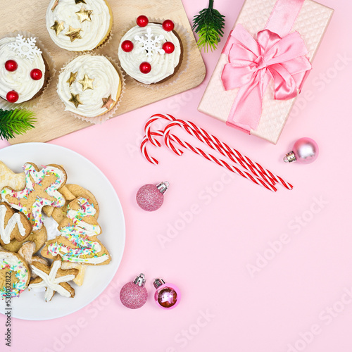 Christmas cup cakes, gingerbread cookies and candy canes on pastel pink background with copy space. Flat lay