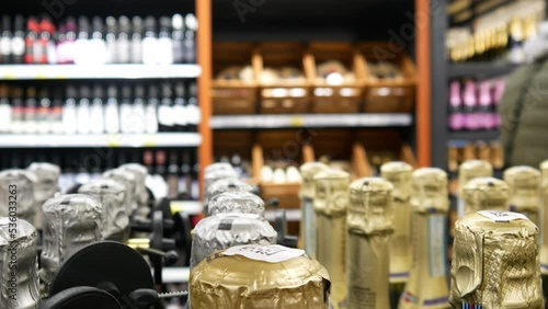 Close-up of many sparkling wine bottles in a liquor store and a buyer walking by with a shopping cart photo