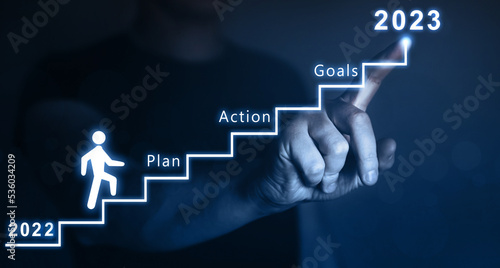 New Year 2023 with plan, action and goals.Businessman pointing to the growing plan of successful business in 2023 year and a figure climbs the ladder of success. 