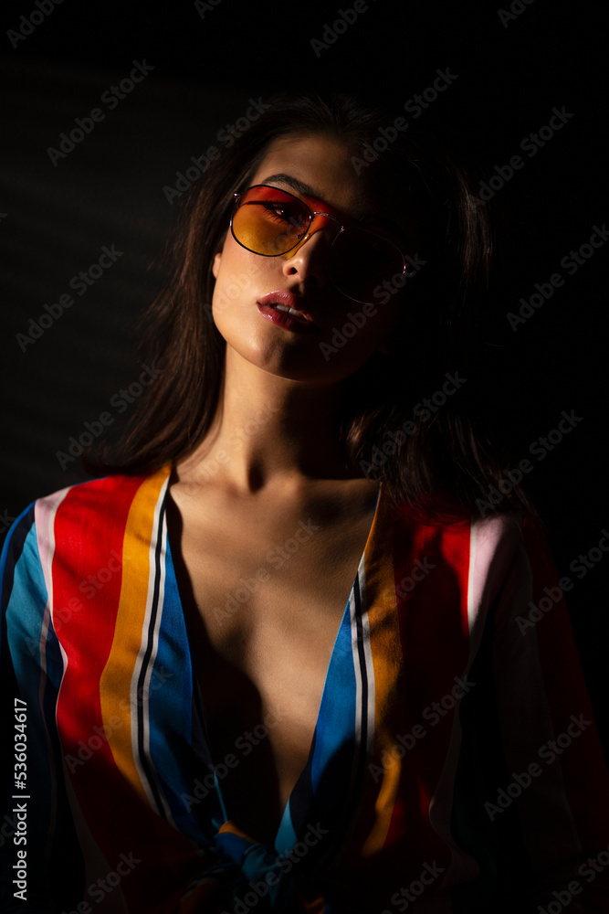 Closeup image of a young brunette woman in colorful clothes and orange sunglasses, isolated black background. Closeup image of a young brunette woman in colorful clothes and orange sunglasses, isolated black background.