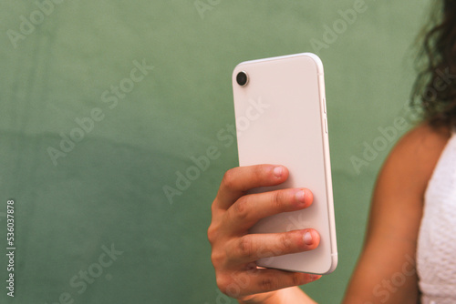 Unrecognizable woman's hand holding a white mobile phone on the background of a green wall.