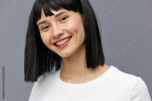 a happy woman stands on a dark background in a tight white T-shirt, smiling broadly with her hands down