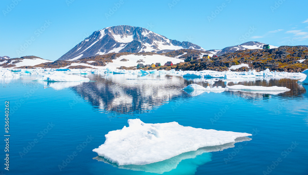 Naklejka premium Panoramic view of colorful Kulusuk village in East Greenland - Kulusuk, Greenland - Melting of a iceberg and pouring water into the sea - Drummer statue in the foreground