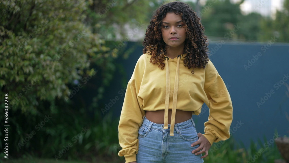 One serious African American young woman standing outside. Portrait of a black hispanic girl with curly hair. South American person One serious African American young woman standing outside. Portrait of a black hispanic girl with curly hair. South American person