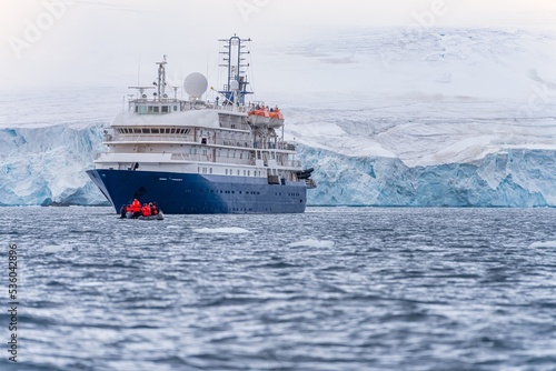 blaues Expeditionsschiff vor antarktischer Eisberg Landschaft in der Cierva Cove - ein tiefer Meeresarm an der Westseite der Antarktischen Halbinsel, umringt von dramatischen Gletscherfronten