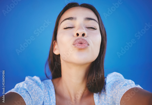 Valokuva Woman face, blowing kiss and selfie portrait blue background for love emoji, relax and flirting on social media