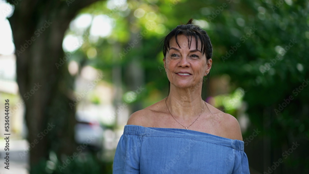 One casual happy older woman walking outdoors in city street. Smiling middle aged 50s lady walks in sidewalk in contemplation One casual happy older woman walking outdoors in city street. Smiling middle aged 50s lady walks in sidewalk in contemplation