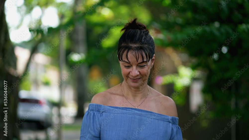 One casual happy older woman walking outdoors in city street. Smiling middle aged 50s lady walks in sidewalk in contemplation One casual happy older woman walking outdoors in city street. Smiling middle aged 50s lady walks in sidewalk in contemplation