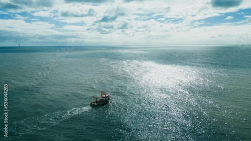 Fishing trawler, boat, ship sailing into the midday sun, trawling for fish off the Lincolnshire coast, near Skegness in the UK. showing boat pulling nets across a deep blue sea. Aerial, video footage photo