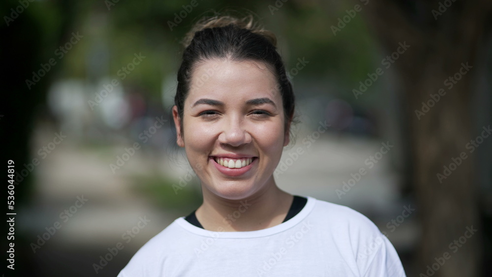Happy young woman portrait face closeup standing outside looking at camera. Casual female person in 20s stands outdoors Happy young woman portrait face closeup standing outside looking at camera. Casual female person in 20s stands outdoors