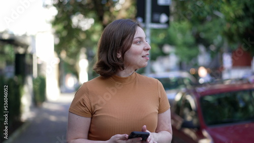 Happy young woman looking at smartphone walking in city street. Girl checking cellphone while going for a walk outdoors in urban sidewalk