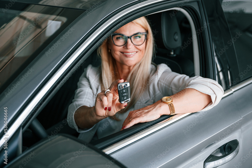 Naklejka premium Sitting inside of the new automobile. Woman in white formal clothes is in the car dealership