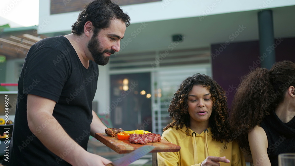 Barbecue chef serving food to friends and family at BBQ home backyard party. Happy people celebrating life with food at lunch holidays Barbecue chef serving food to friends and family at BBQ home backyard party. Happy people celebrating life with food at lunch holidays