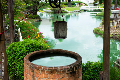 Classic vintage retro antique stone brick artesian water well and roof and wooden bucket reel with rope for thai people use at outdoor garden park at rural countryside in Nonthaburi, Thailand photo