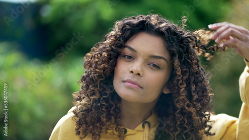 A black hispanic latina girl adjusting curly hair looking at camera. Portrait face closeup of young woman
