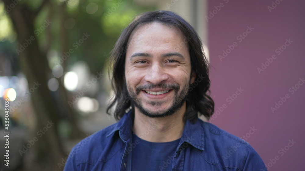 A happy hispanic man walking forward smiling. South American Brazilian person portrait face closeup in urban city street in daylight A happy hispanic man walking forward smiling. South American Brazilian person portrait face closeup in urban city street in daylight