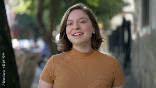 Portrait of a happy young woman walking in city sidewalk. Millennial girl in 20s walks forward feeling confidence