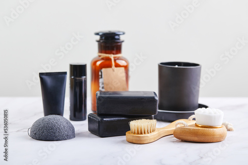 Three pieces of black charcoal soap, Konjac sponge, beauty care products, candles and brushes for washing and massage on marble background