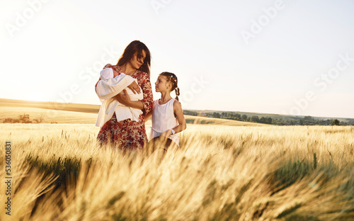 Standing together. Mother with her newborn baby and girl is on the field at sunny day