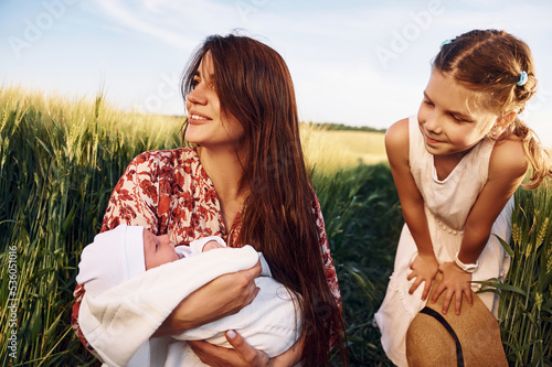 Looking at the newborn baby. Mother with girl is on the field at sunny day together