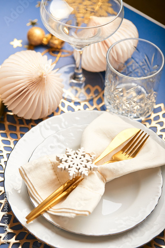 Christmas festive table setting with white plates and gold cutlery, gifts in white and gold paper, decorations and balls.