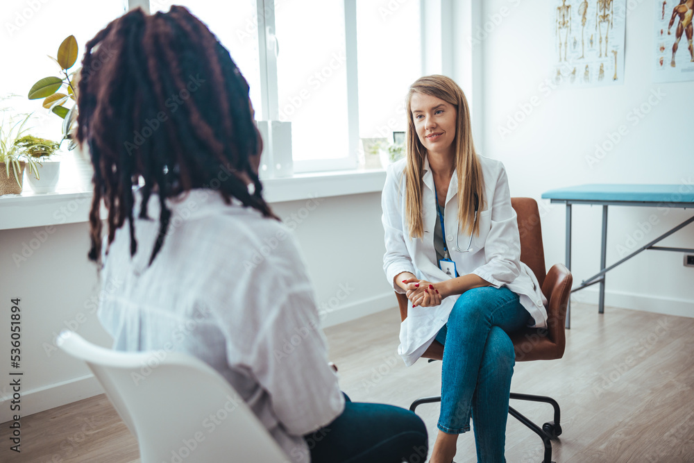 A young female of African ethnicity sits on the examination table at her gynaecologist's office. She is talking to her doctor about her health history. Doctor is checking patient symptom A young female of African ethnicity sits on the examination table at her gynaecologist's office. She is talking to her doctor about her health history. Doctor is checking patient symptom