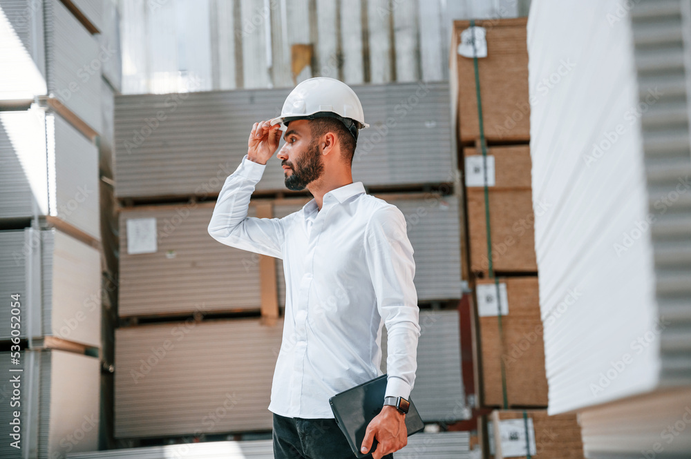 In white hard hat. Storage worker is in the warehouse with bunch of products In white hard hat. Storage worker is in the warehouse with bunch of products