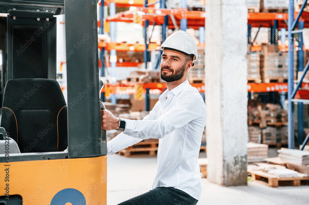Using cargo moving machine. Storage worker is in the warehouse with bunch of products Using cargo moving machine. Storage worker is in the warehouse with bunch of products