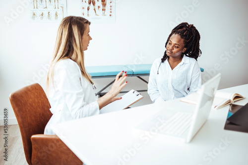 Doctor listens as a female patient discusses her health. A young female patient sits casually with her doctor as they discuss her mental health. She is seated in a chair in front of her doctor 