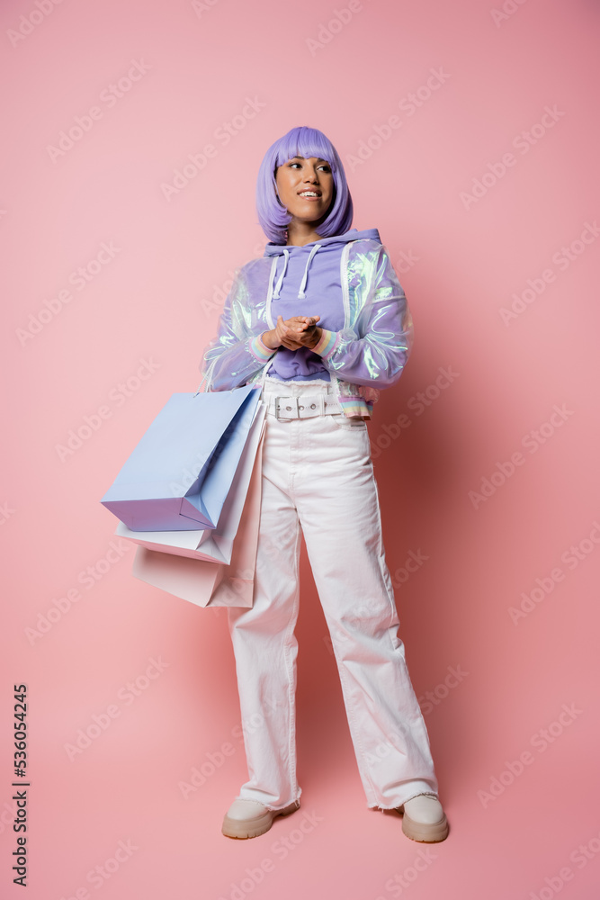 full length of joyful african american woman in transparent jacket standing with shopping bags on pink. full length of joyful african american woman in transparent jacket standing with shopping bags on pink.