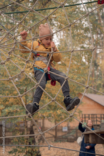 Happy boy cheering while climbing a net. Child crawling on rope mesh at playground. High quality photo
