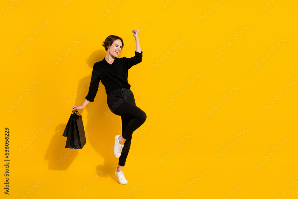 Full length photo of hooray young lady hold bags yell wear shirt jeans boots isolated on yellow color background