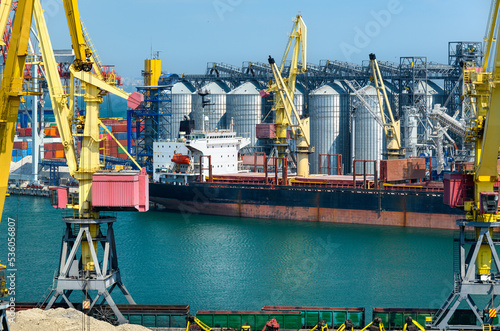 industrial seaport infrastructure, sea, cranes and dry cargo ship, grain silo, bulk carrier vessel and grain storage elevators, concept of sea cargo transportation