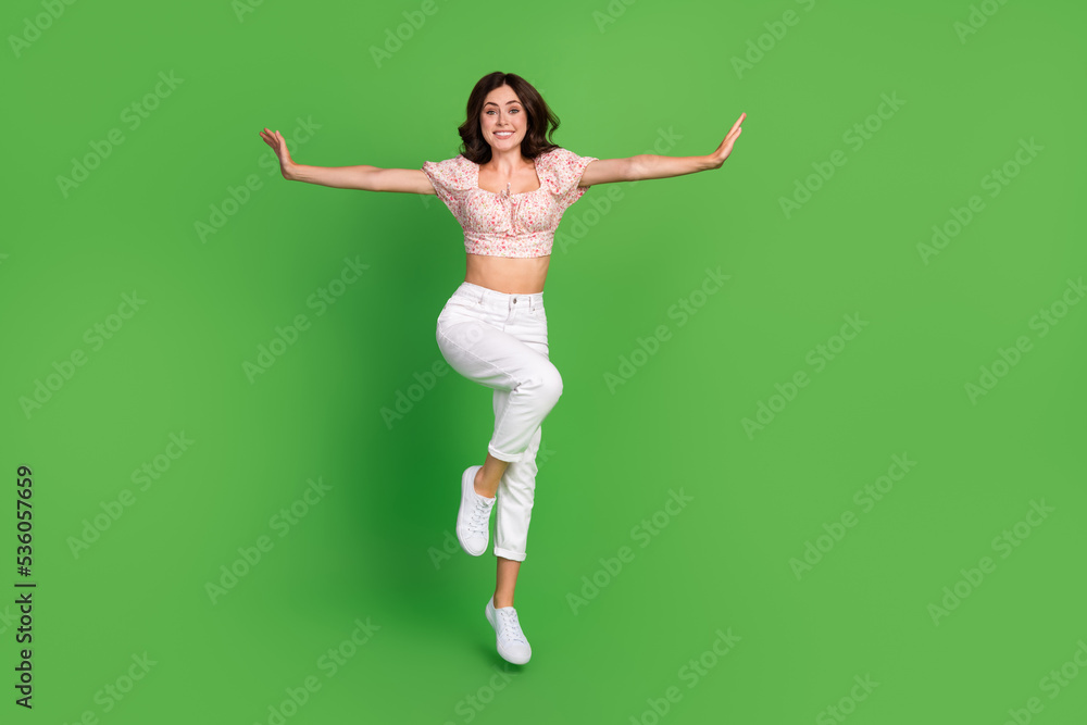 Fototapeta premium Full length photo of adorable cute girl dressed print blouse arms sides jumping high isolated green color background