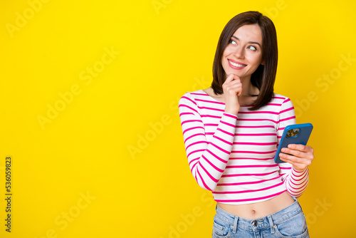 Photo of gorgeous adorable girl brunette hairdo dressed striped shirt look at empty space hand chin isolated on yellow color background