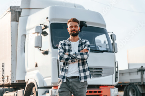 With arms crossed. Young truck driver is with his vehicle at daytime