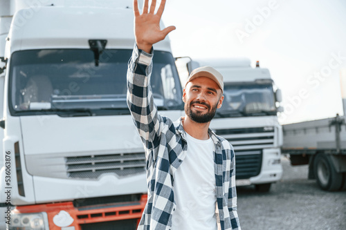Showing hello gesture by hands and smiling. Young truck driver is with his vehicle at daytime © standret