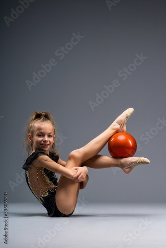 A young girl gymnast in a gymnastic leotard does exercises with a ball. Isolated on a gray background. photo
