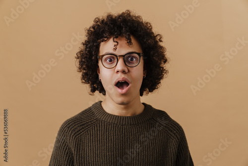 Young handsome curly shocked boy in glasses and sweater