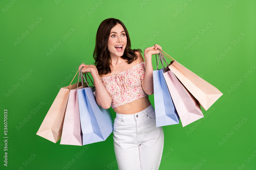 Photo of shiny impressed girl dressed print blouse holding bargains looking empty space isolated green color background Photo of shiny impressed girl dressed print blouse holding bargains looking empty space isolated green color background