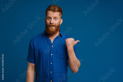 Adult handsome stylish redhead bearded surprised man poitning aside photo