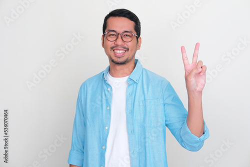 Adult Asian man smiling friendly while giving two fingers sign