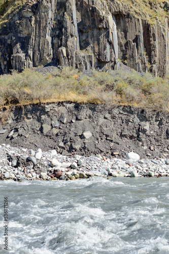 White water of the  mountain stream in summer time. Torrent waves, white and brown stones, green grass rocky slopes on the bank
