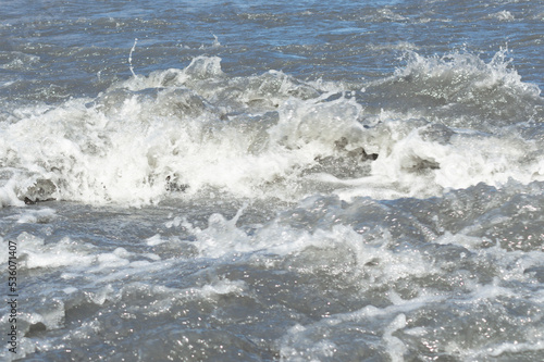 Close-up white water of the mountain stream in a summer day. White and grey foam of waves and drops of water