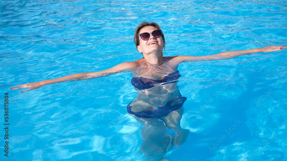 Portrait of smiling girl in sunglasses in swimsuit swims in pool