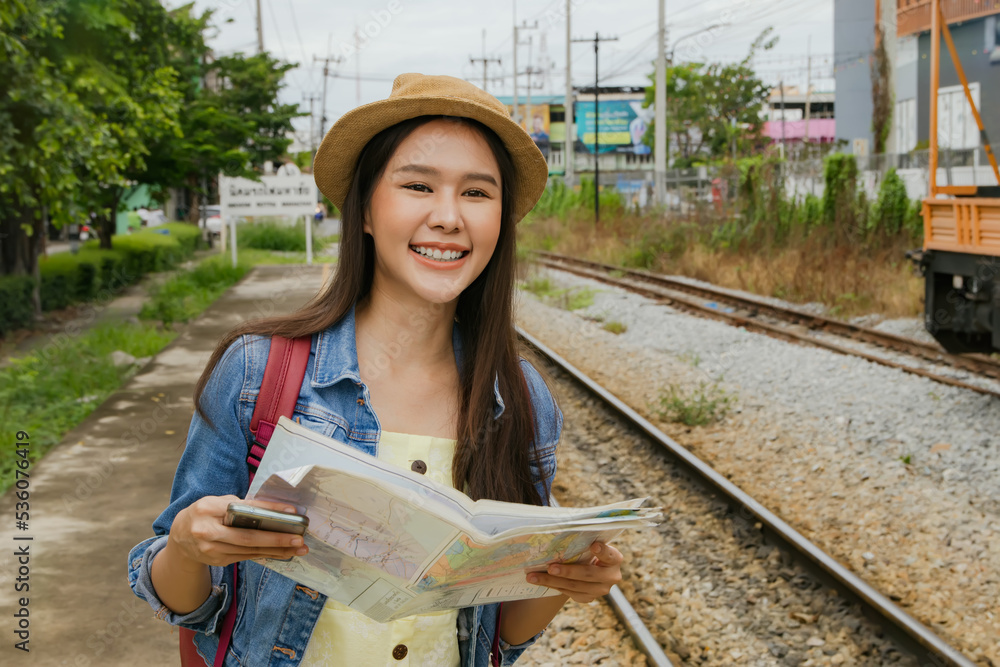 Beautiful Asian woman excitedly looks at an interesting tourist map. while waiting for the train at the suburban station to pick her up at the departure and the special train journey.