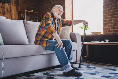 Photo of stressed unhappy man pensioner wear checkered shirt holding walking cane trying standing up sofa indoors house room © deagreez