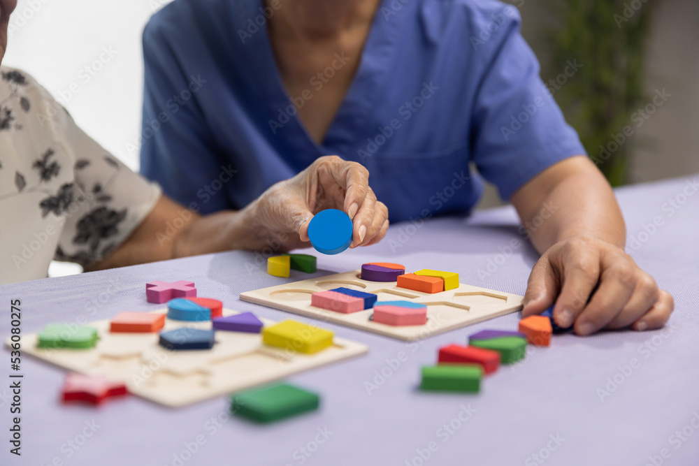 Caregiver and senior woman playing wooden shape puzzles game for dementia prevention - obrazy, fototapety, plakaty 