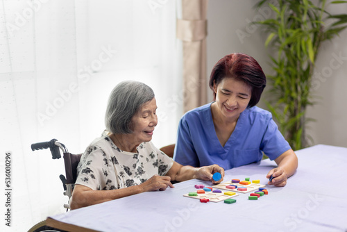 Caregiver and senior woman playing wooden shape puzzles game for dementia prevention photo